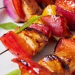 Pinterest graphic of a close up view of Hawaiian chicken skewers with chicken, bell peppers, and red onions.