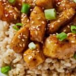 Pinterest graphic of a close view of honey garlic chicken bites over a bed of rice with green onion garnish.