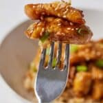 Pinterest graphic a fork with two pieces of honey garlic chicken bites with sesame seeds and green onions.