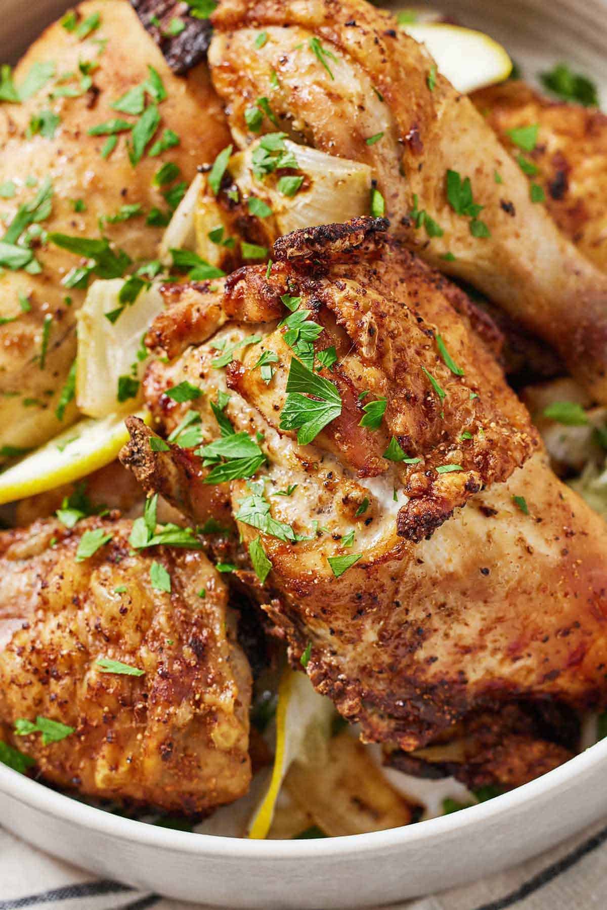 Close up view of air fryer Lebanese chicken with slices of lemon and fresh chopped herbs.