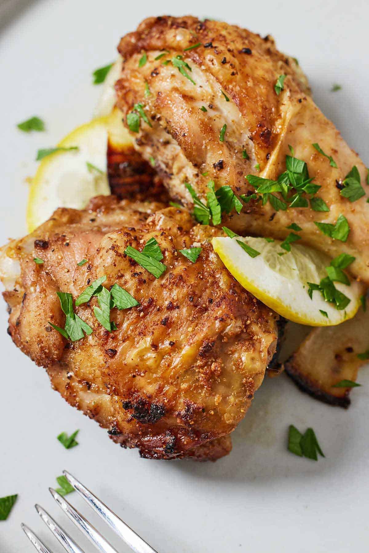 Overhead view of two pieces of air fryer Lebanese chicken with sliced lemon and chopped herbs on a plate.