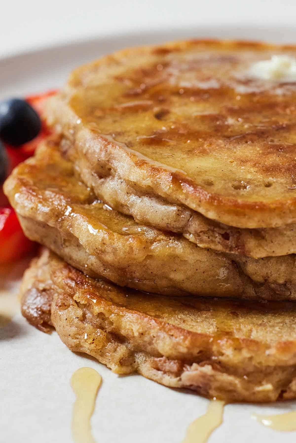 A profile view of a stack of three apple pancakes with syrup drizzled over.
