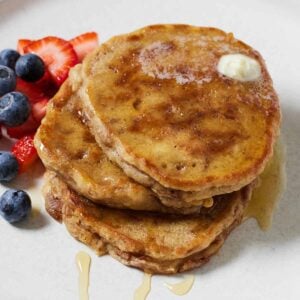 An angled view of three apple pancakes with syrup drizzled over top and fresh berries on the side.