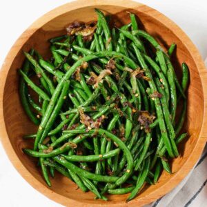 Overhead view of a wooden bowl of crispy shallot green beans.