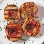 Overhead view of four grilled peaches on a white plate with fresh mint.