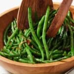 Pinterest graphic of a bowl of crispy shallot green beans being lifted with two wooden serving spoons.