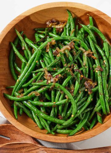 Overhead view of a wooden bowl with crispy shallot green beans.