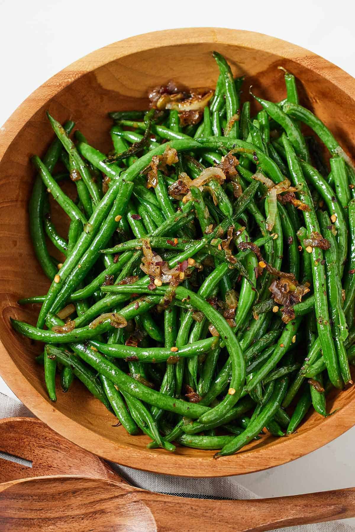 Overhead view of a wooden bowl with crispy shallot green beans.