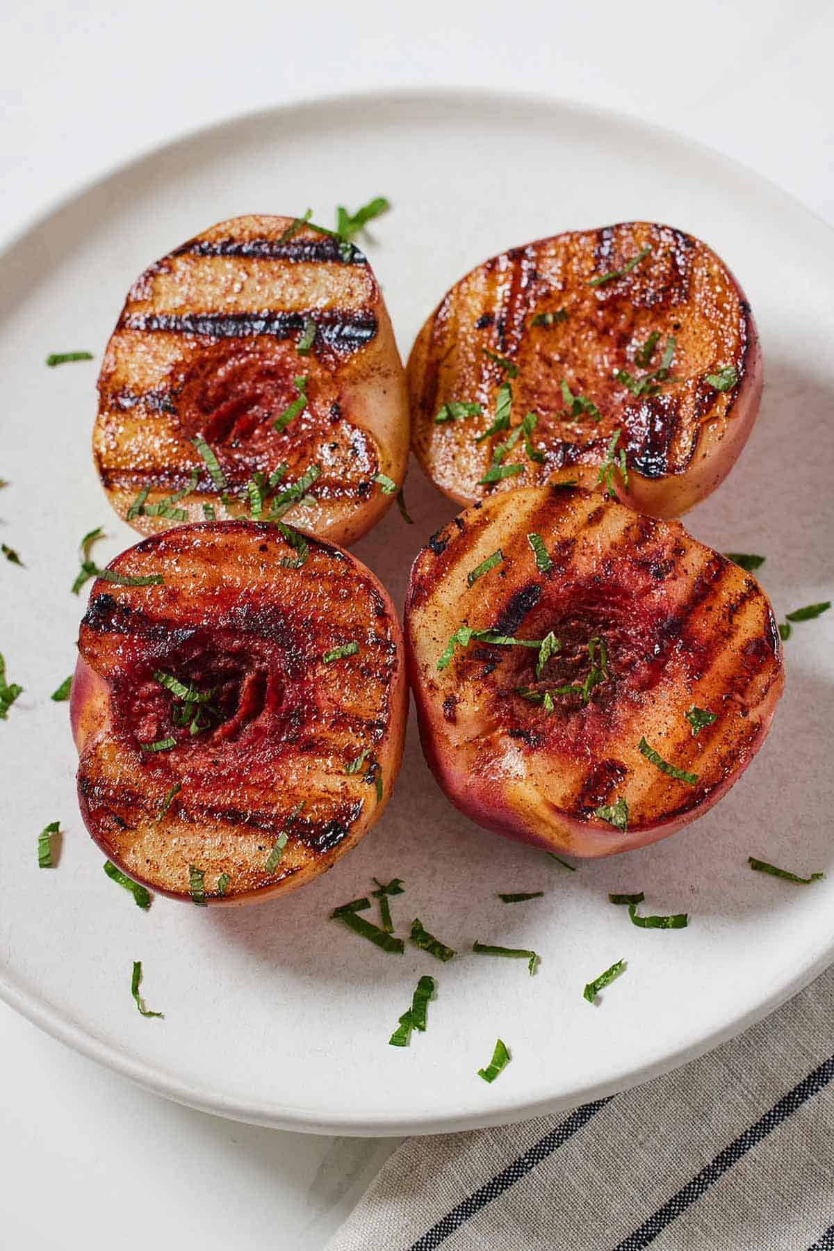 A plate with four grilled peaches with fresh chopped mint leaves as garnish.
