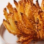 Pinterest graphic of a close up, profile view of an air fryer blooming onion on a plate.