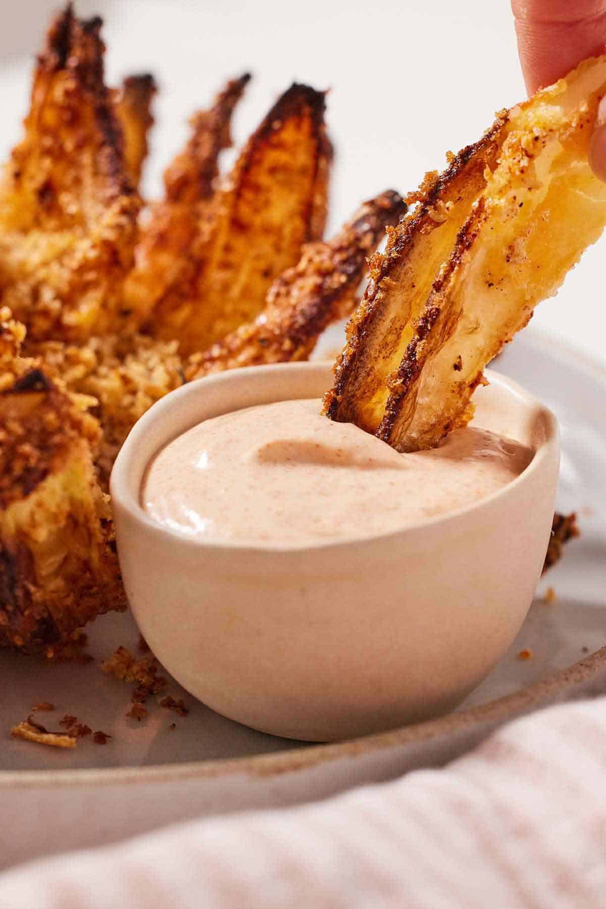 A piece of air fryer blooming onion dipped into a small bowl of sauce.