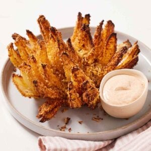 An air fryer blooming onion on a plate with a dip on the side.