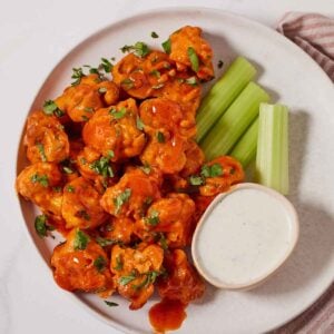 A plate with air fryer cauliflower wings, celery, and a small bowl of dip.