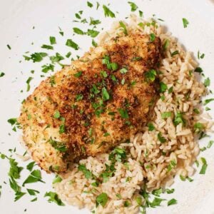 Overhead view of air fryer parmesan crusted chicken with a side of brown rice with chopped parsley on top.