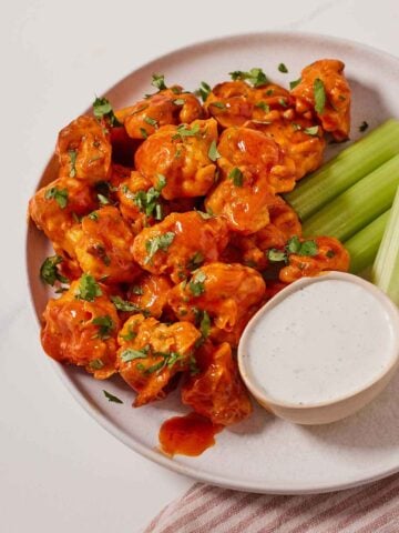 A plate with air fryer cauliflower wings, celery, and dipping sauce with fresh herb on top.