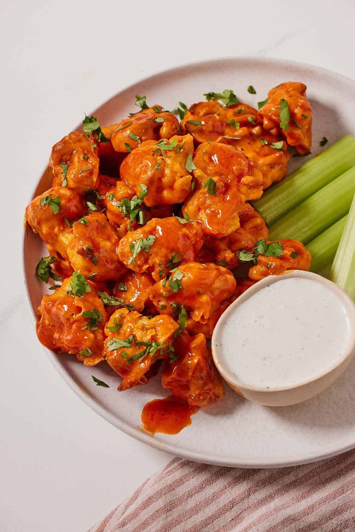 A plate with air fryer cauliflower wings, celery, and dipping sauce with fresh herb on top.