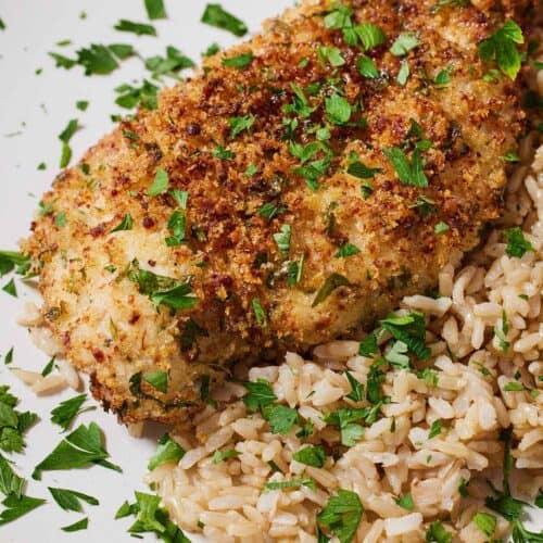 A plate of rice and air fryer parmesan crusted chicken with fresh chopped herbs on top.