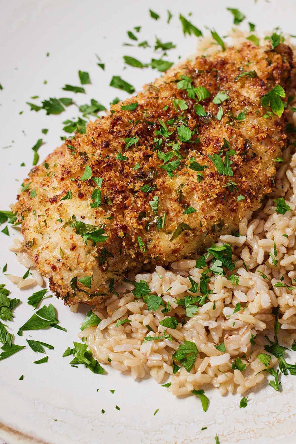 A plate of rice and air fryer parmesan crusted chicken with fresh chopped herbs on top.