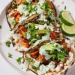 Pinterest graphic of a plate of three sweet potato tacos with garnishes and sauce on top.