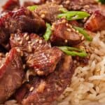 Pinterest graphic of a close up view of air fryer steak bites with sesame seeds and green onions over some rice.