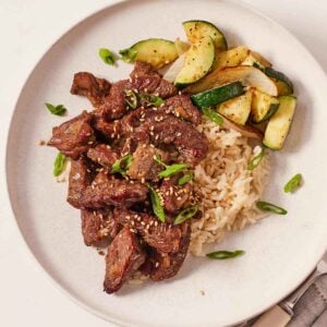 Overhead view of air fryer steak bites on a plate with rice, zucchini, and onions.