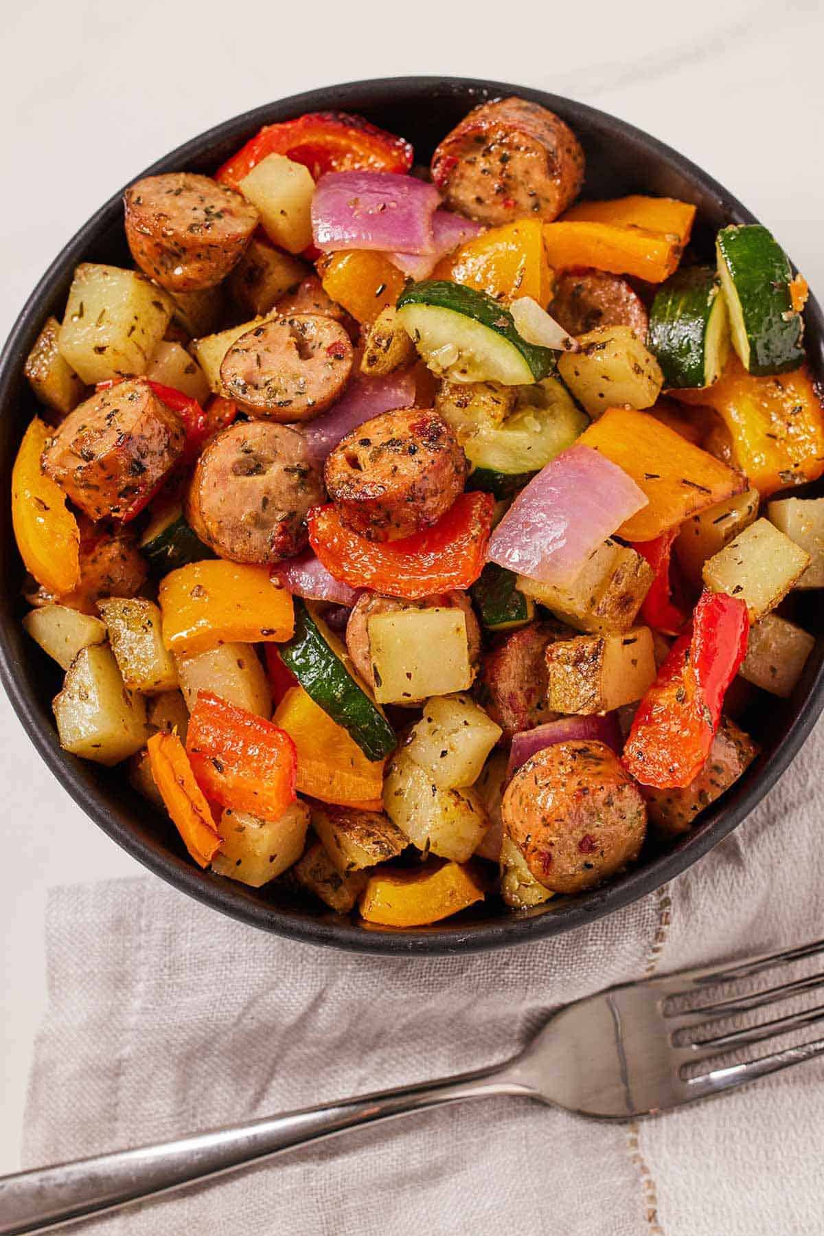 A bowl of air fryer sausage and vegetables with a fork on the side.