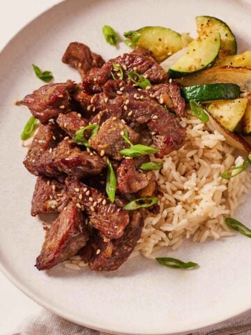 A plate with air fryer steak bites along with rice, zucchini, and onions.