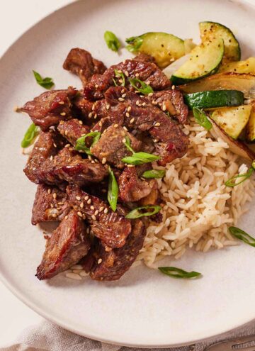 A plate with air fryer steak bites along with rice, zucchini, and onions.