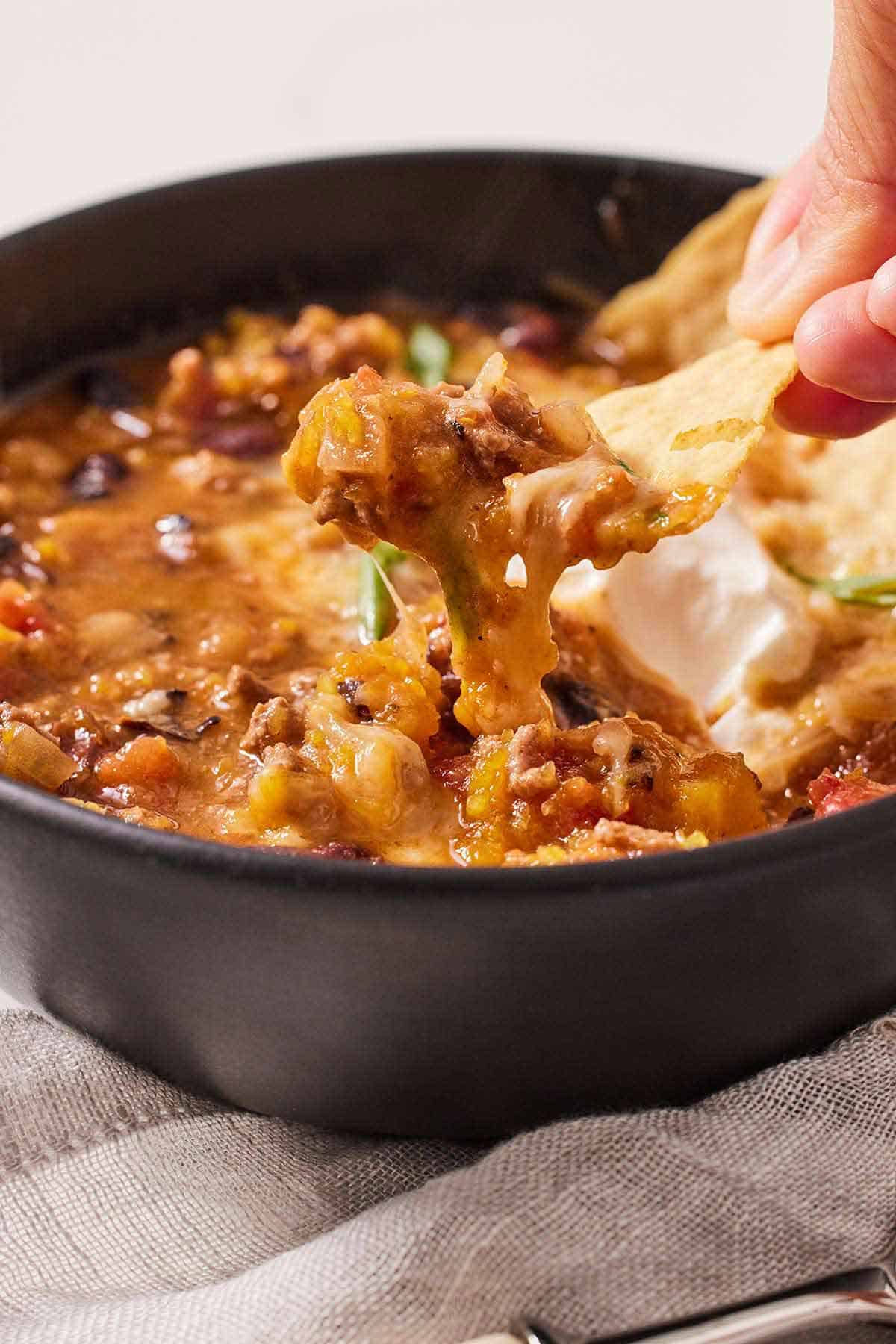 A bowl of butternut squash chili with a chip scooping out some.