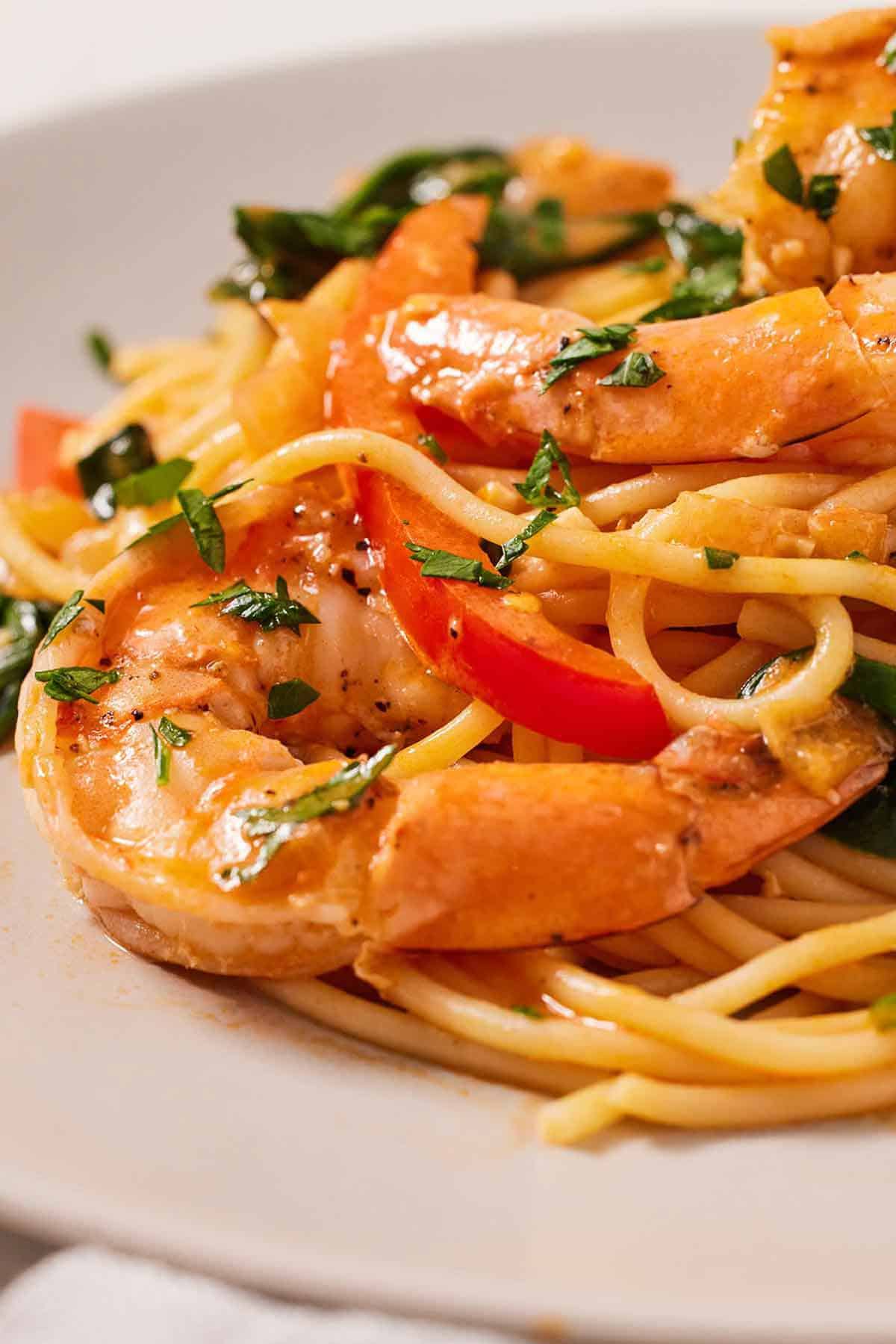 Close up of a piece of shrimp on a plate of red curry pasta.
