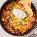 Pinterest graphic of an overhead view of a bowl of butternut squash chili with a scoop of sour cream and two tortilla chips.