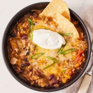 Overhead view of a bowl of butternut squash chili with two chips and a dollop of sour cream.