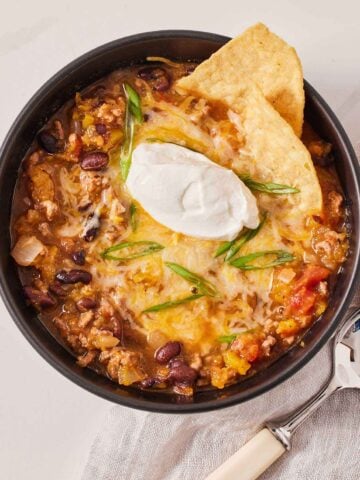 Overhead view of a bowl of butternut squash chili with tortilla chips and sour cream on top.