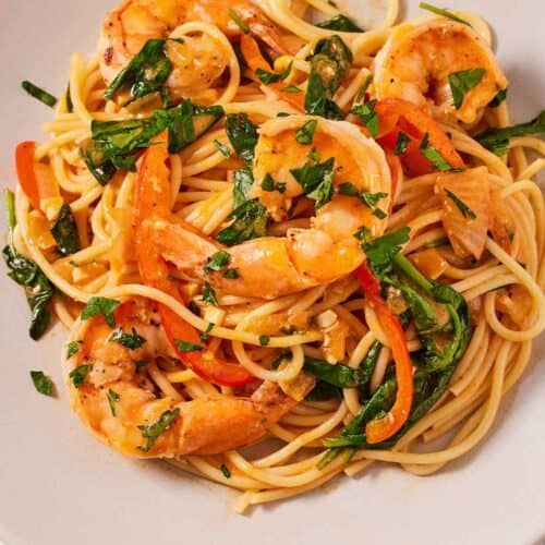 Overhead view of a plate of red curry pasta with shrimp with fresh chopped herb garnish.