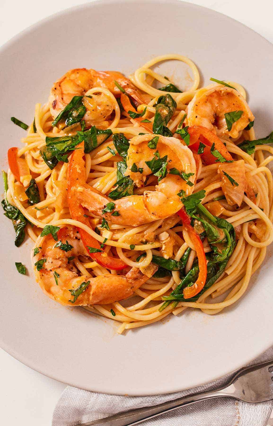 Overhead view of a plate of red curry pasta with shrimp with fresh chopped herb garnish.