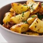 Pinterest graphic of a profile view of a bowl of air fryer Greek lemon potatoes topped with parsley.