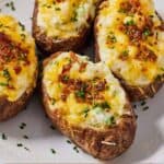 Pinterest graphic of a plate with four air fryer twice baked potatoes with chives and bacons sprinkled on top.