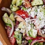 Pinterest graphic of a close up overhead view of a bowl of avocado Greek salad with tomatoes, cucumbers, red onions, and feta.