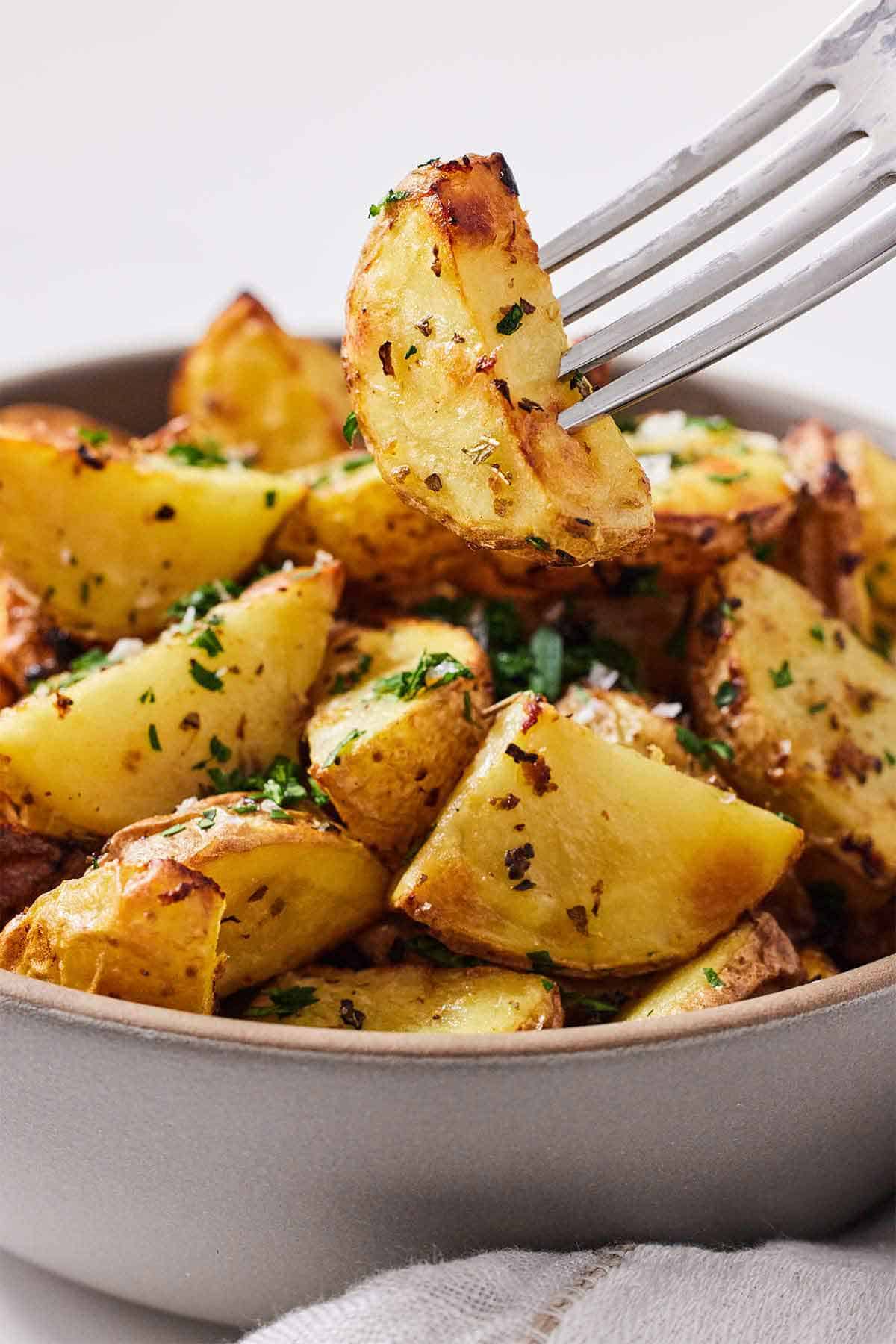 A fork lifting up a piece of air fryer Greek lemon potato from the bowl.