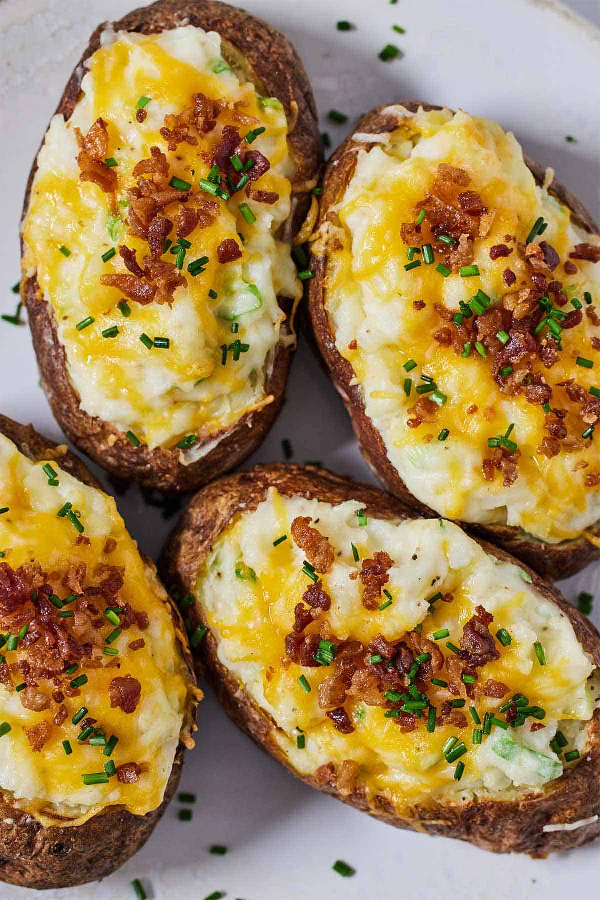 Overhead view of four air fryer twice baked potatoes topped with chives and bacon bits.