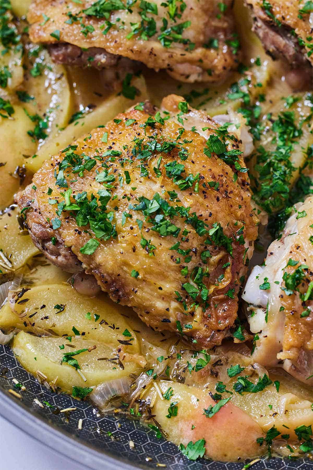 Overhead view of apple cider chicken over cooked apples in a skillet with parsley on top.