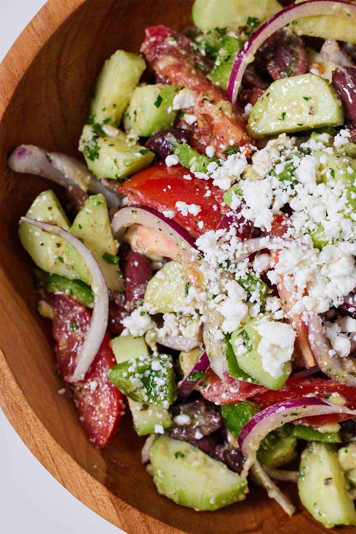 Close up of a bowl of avocado Greek salad with feta crumbled on top.