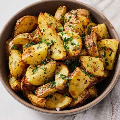 A bowl of air fryer Greek lemon potatoes with chopped parsley on top.