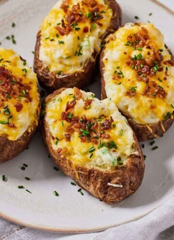 A plate with four air fryer twice baked potatoes topped with chives and bacon bits.